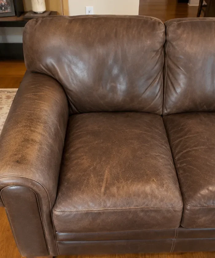 Leather sofa with scuffs, stains and worn patches before professional cleaning